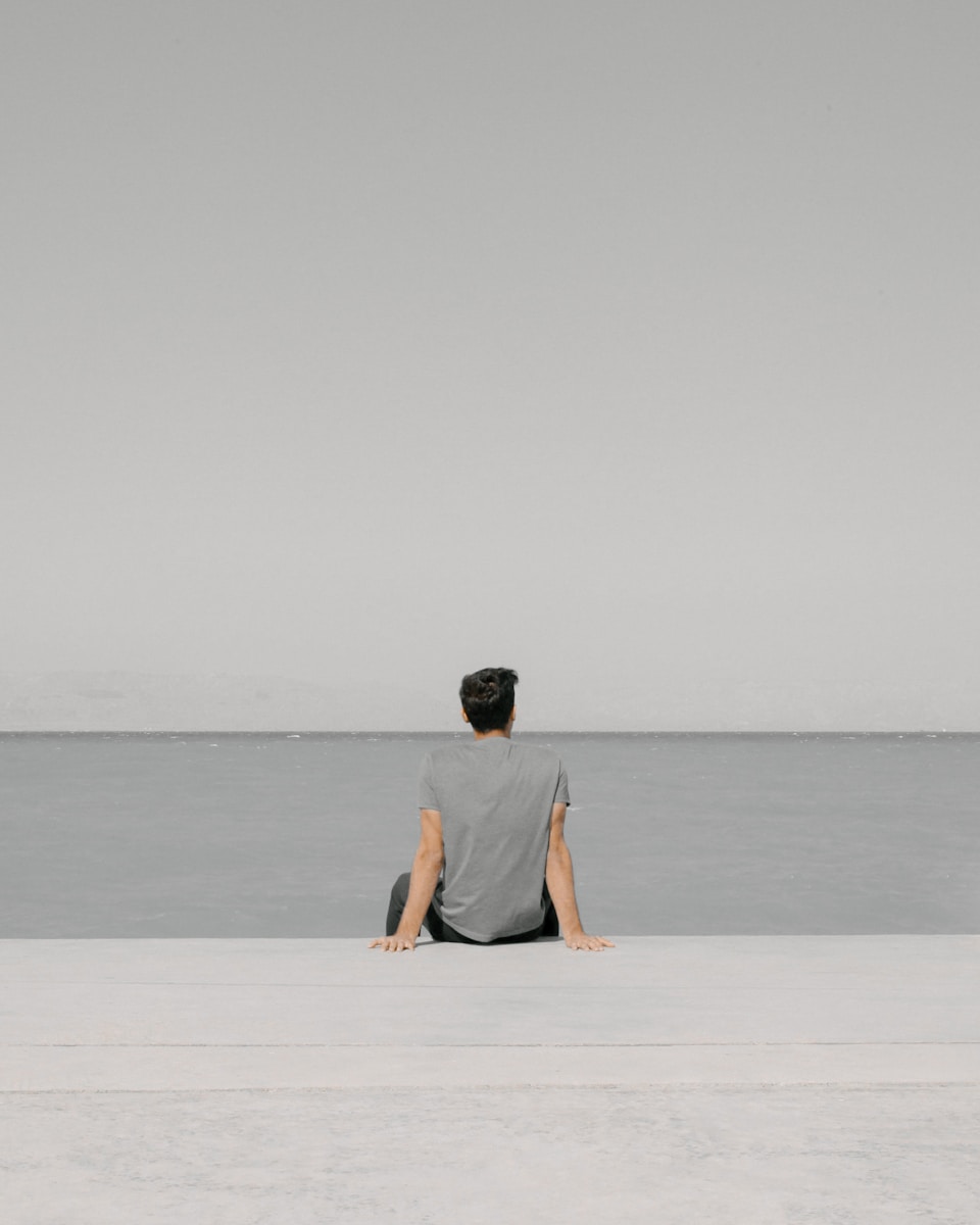 man in yellow shirt and black shorts sitting on white sand near body of water during