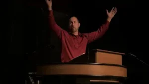 Bryan Murawski at chapel podium with hands raised