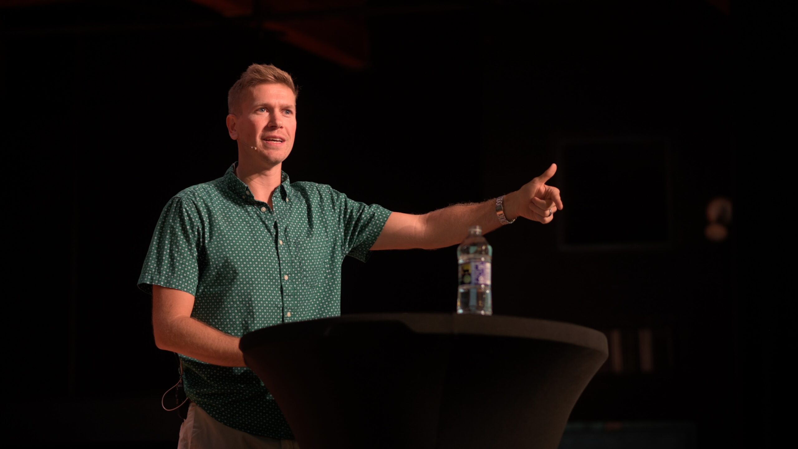 Adam Derus standing on chapel stage next to a high-top table