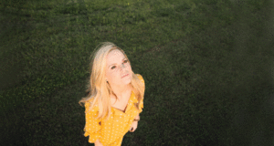 Photo of a blonde woman in a yellow dress staring up at the sky