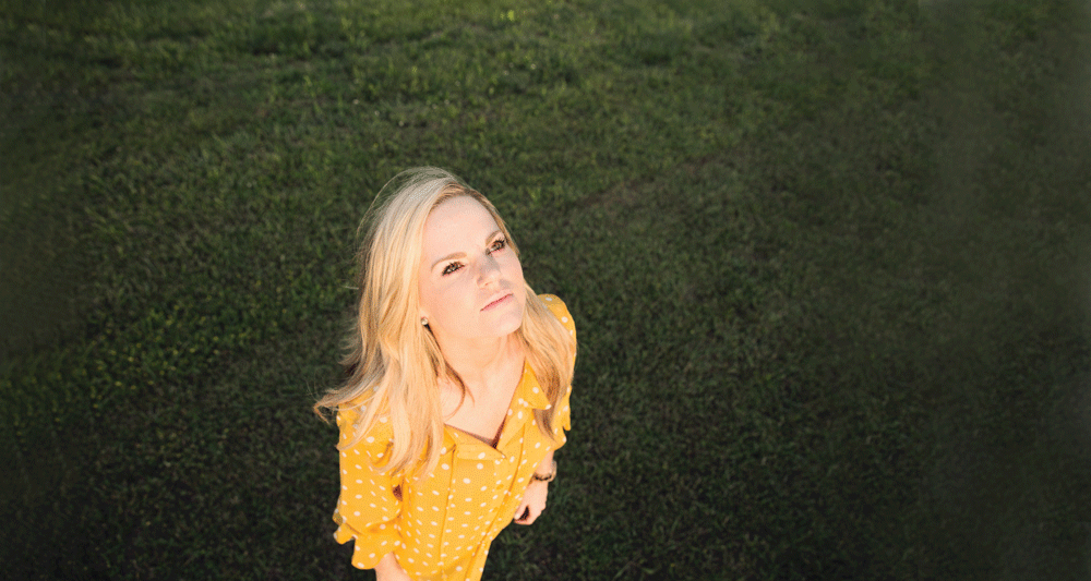 Photo of a blonde woman in a yellow dress staring up at the sky