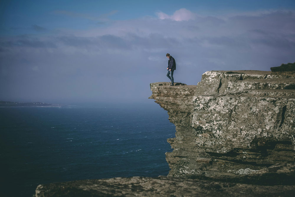 man in standing on the edge of a cliff overlooking a large expanse