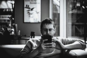 black and white image of man sitting on a couch, absorbed in his phone screen, which he is holding near his face