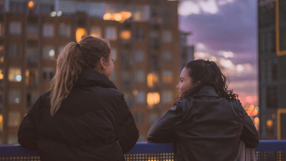 two women having a conversation while looking over city skyline
