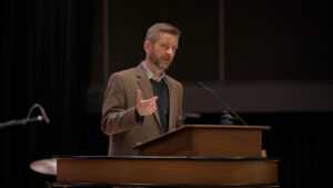 Dr. Joshua Brownfield speaking at chapel podium with one hand raised