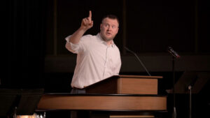Jon Shepherd standing behind chapel podium with finger pointing in the air