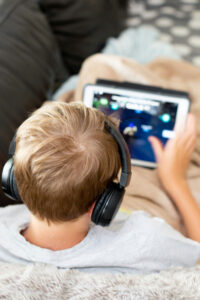 image from behind a boy reclining on a couch wearing headphones and holding a tablet