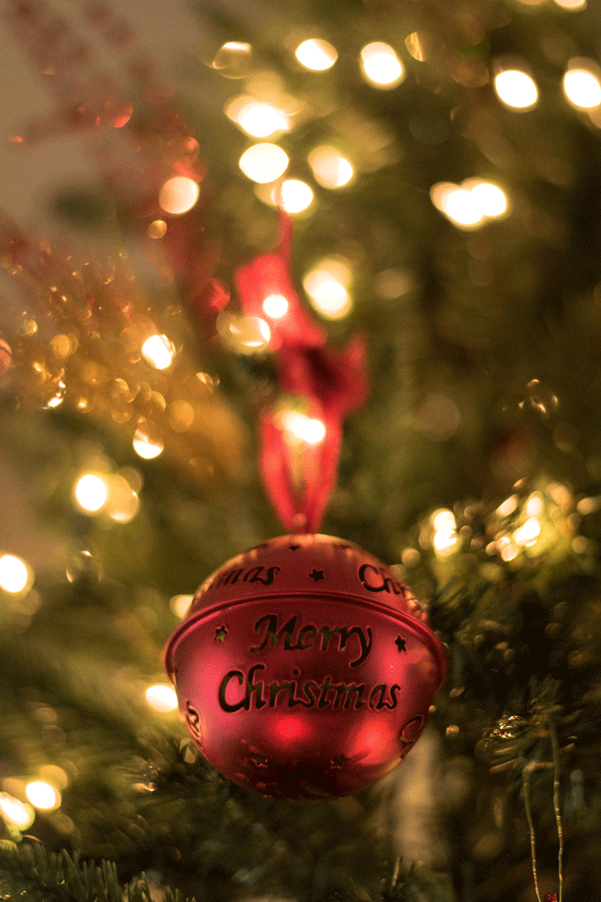 red sleigh bell ornament on a tree, inscribed with "Merry Christmas"