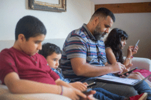 dad and three kids sitting next to each other on a couch, all absorbed in their own tech device
