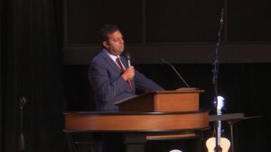 Dr. Ayman Ibrahim behind chapel podium holding a microphone