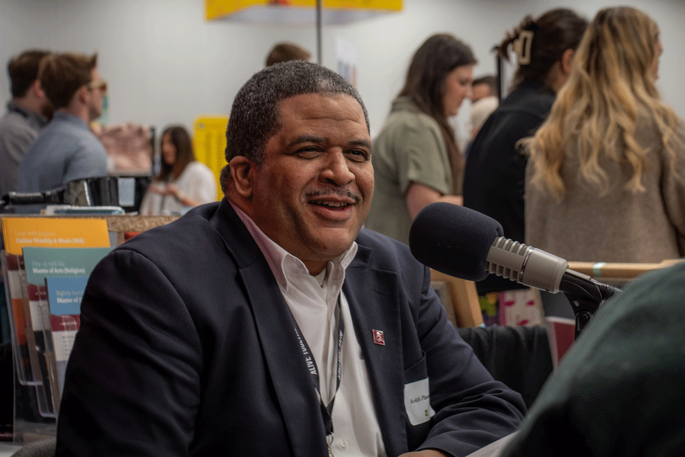 Dr. Keith Plummer smiles as he talks into a podcast mic