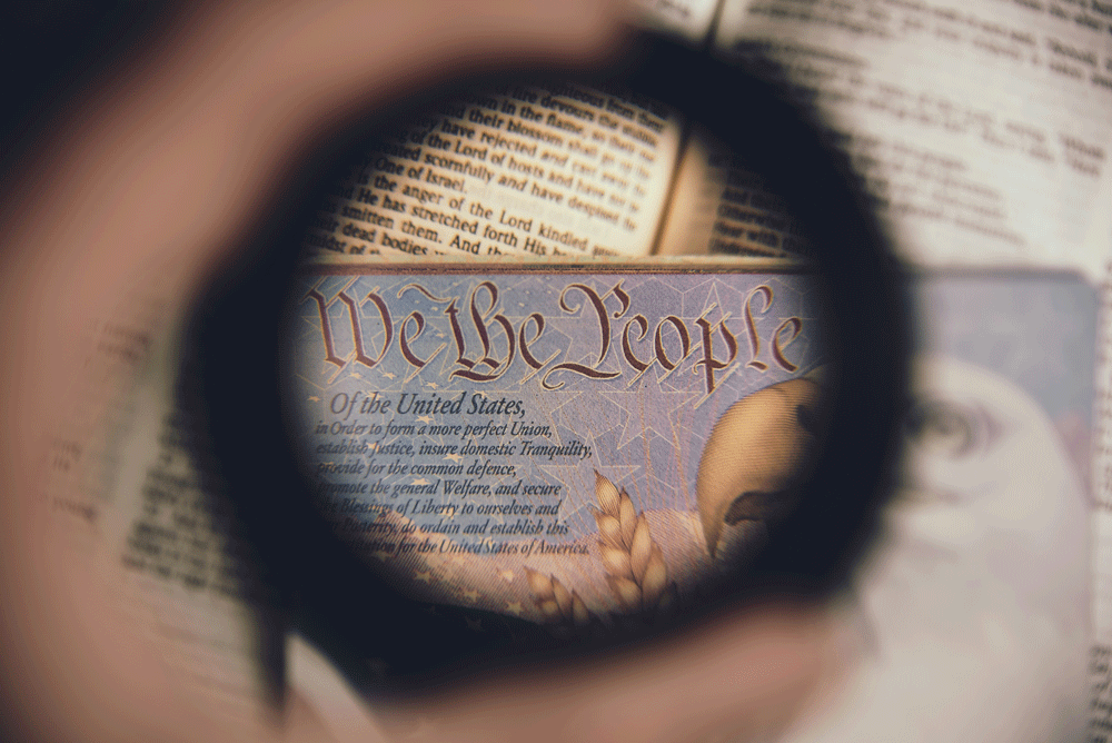Image of a hand holding a ring, with "we the people" in view on the document in the background