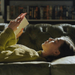 woman lying on a couch holding an open book