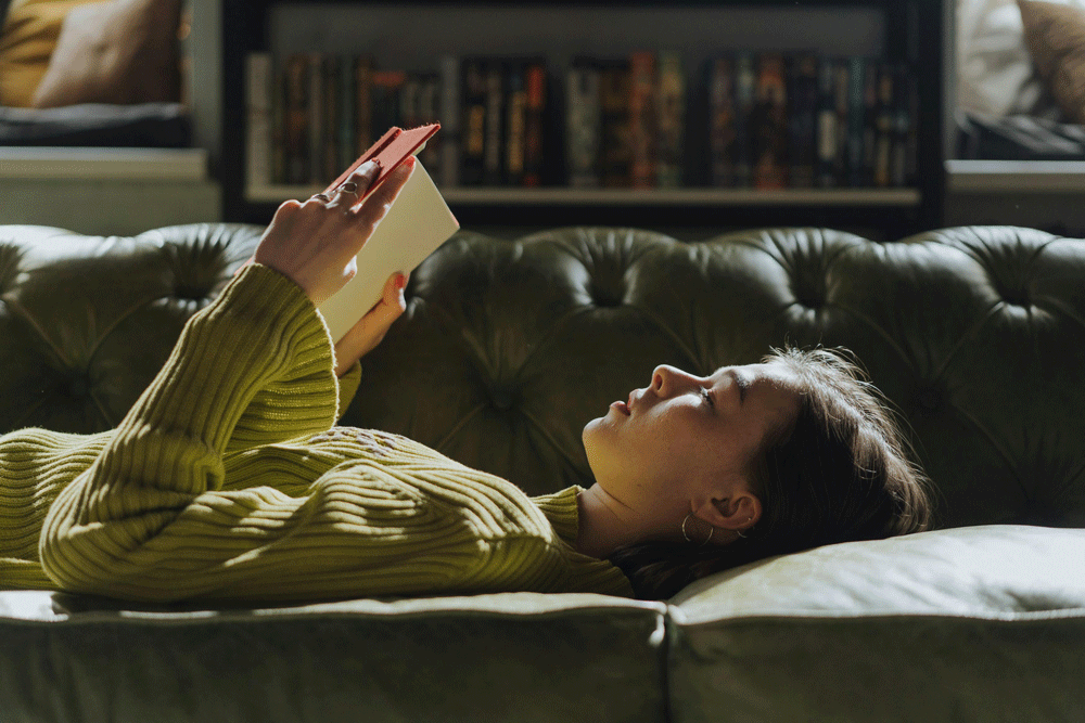 woman lying on a couch holding an open book
