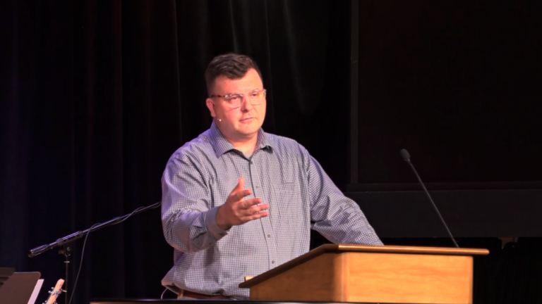 Andrew Gordon standing behind chapel podium with one arm raised in the air