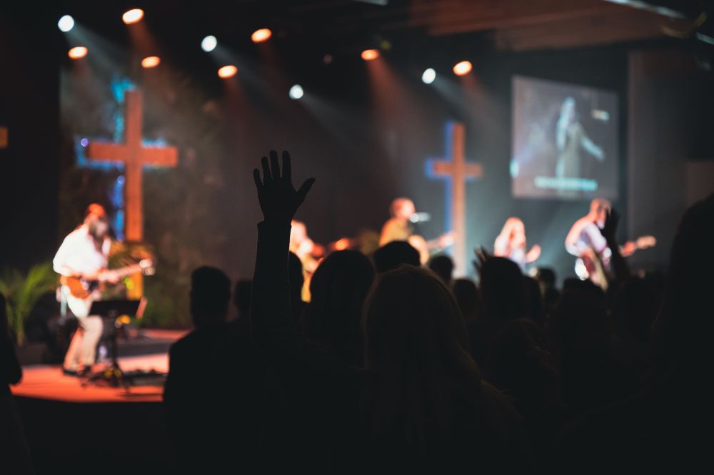 image of shadowed congregants worshiping in a church with band members on stage