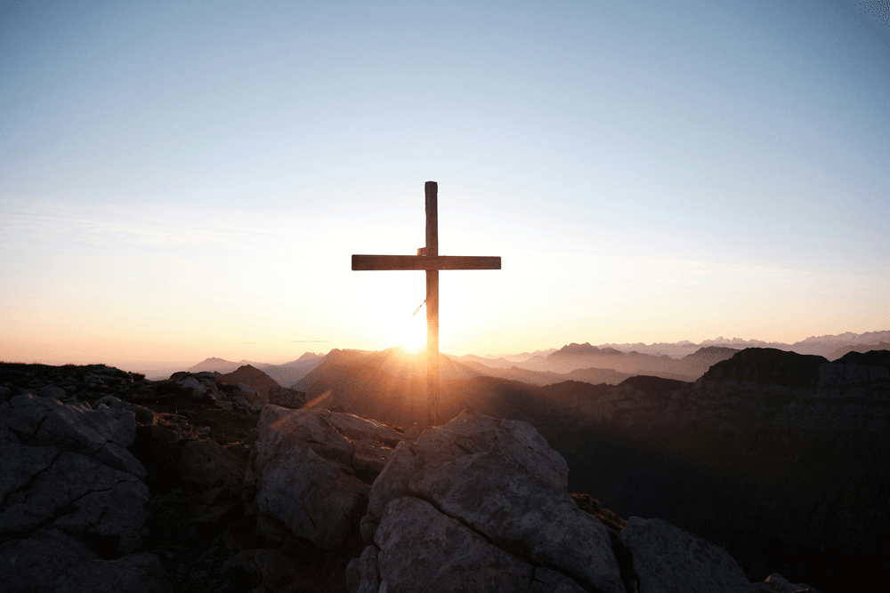 image of a cross on the top of a hillside at sunrise